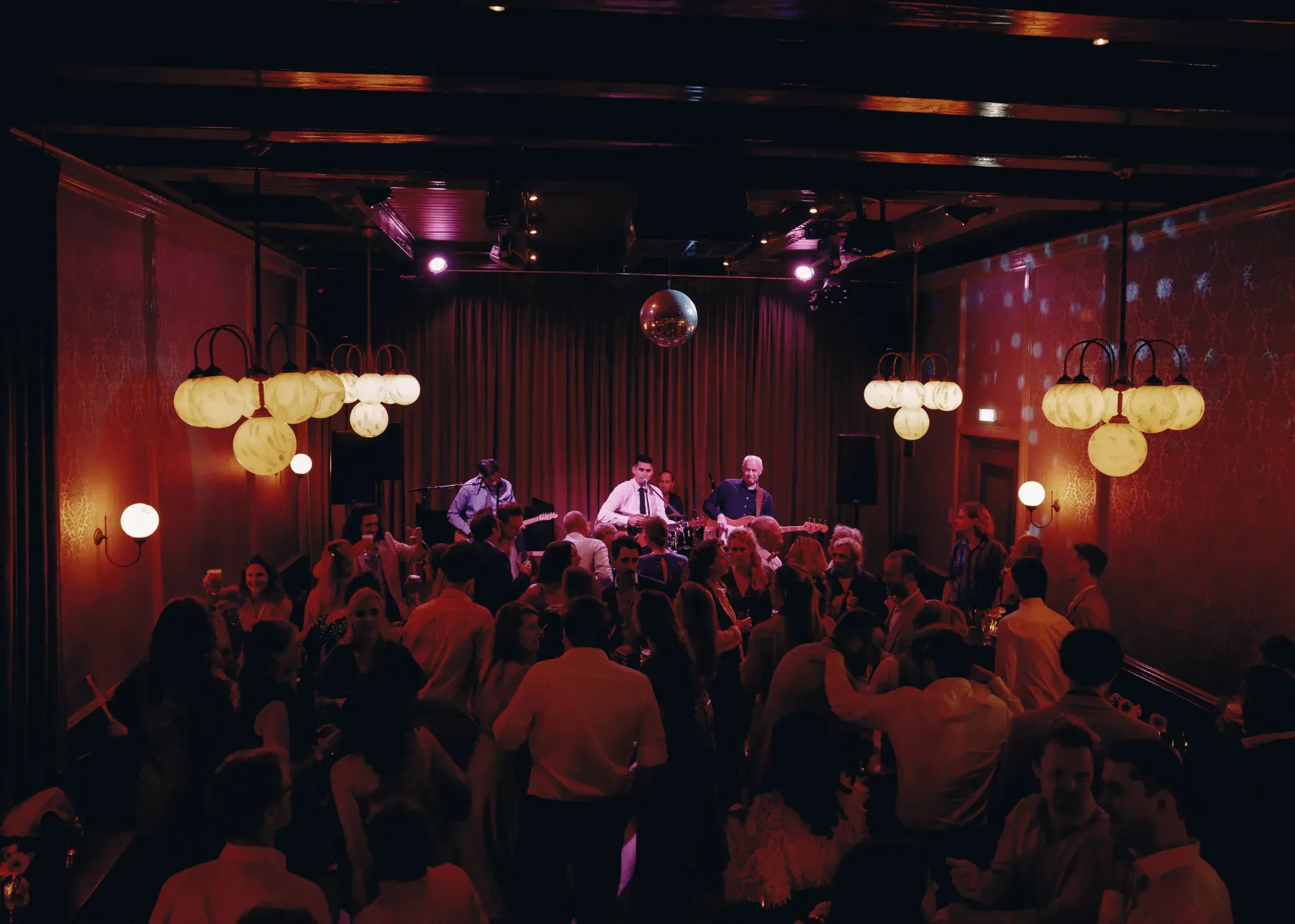 Een band speelt op het podium in een volle Grote Zaal van Het Broeker Huis in Broek in Waterland tijdens een bruiloft met een dicobol boven de dansvloer